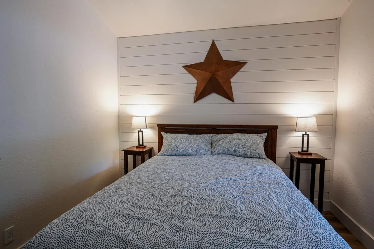 A cozy bedroom with a plush bed framed by bedside lamps and a striking star wall decoration. Soft natural light filters through the room, creating a restful atmosphere perfect for unwinding after a day of adventure.