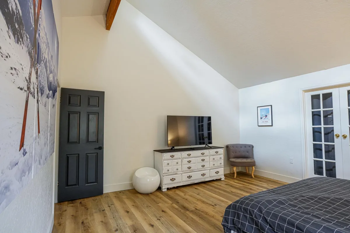 The scene centers on a wall-mounted TV, an armchair, a dresser, and ski-themed wall art, all arranged in a modern, cozy space. The image exudes a sense of comfort and is clearly set up for entertainment, making it an inviting spot for movie nights or catching up on shows.