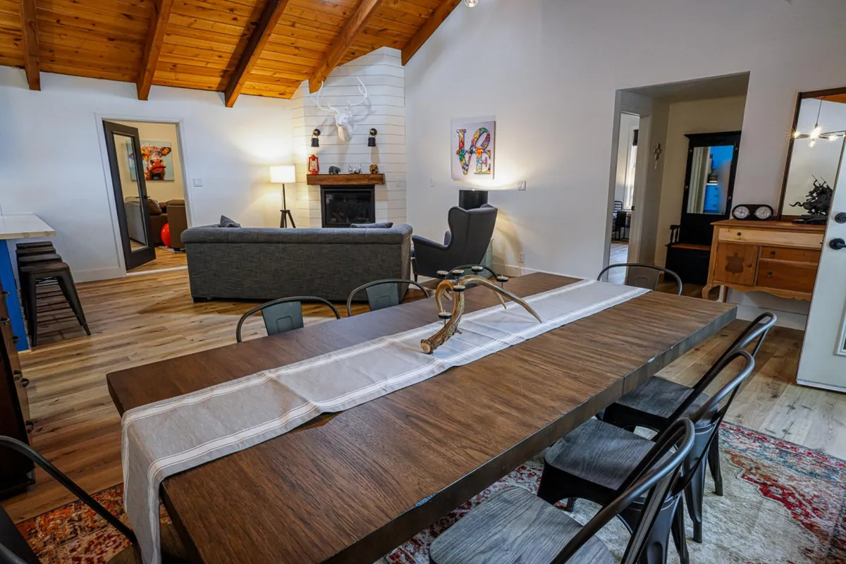 The dining area is the centerpiece here, featuring a large dining table set near a cozy fireplace, with artwork on the wall and a sofa visible in the background. The inviting atmosphere is ideal for memorable family dinners, game nights, and heartfelt conversations.