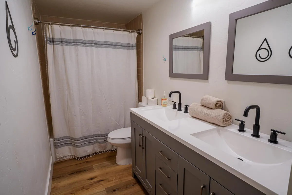 A bright, fresh bathroom with a double sink vanity, decorative mirrors, and a shower curtain. The space is designed for morning rituals and self-care, offering guests a comfortable place to refresh and unwind.
