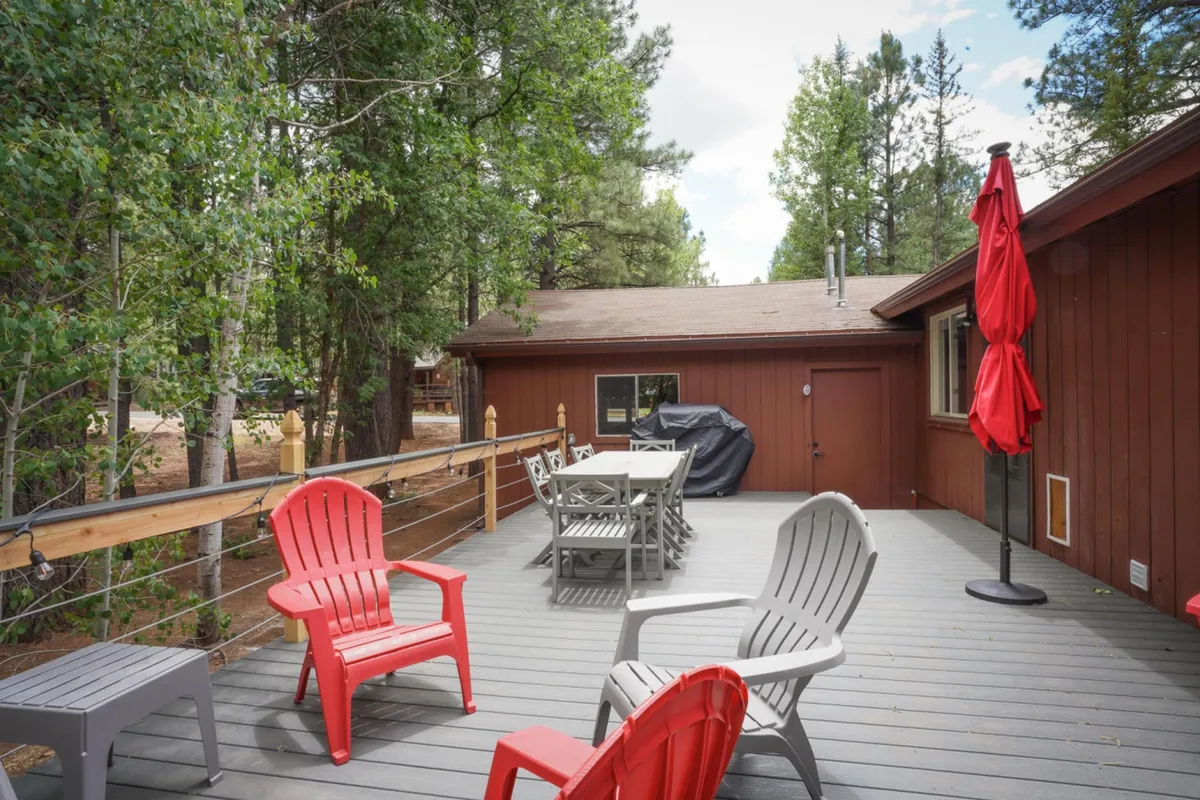 A backyard scene featuring red Adirondack chairs, an outdoor dining table, and a grill, all set on a deck with views of trees beyond. The cozy setup encourages barbecues, sunset watching, and stargazing—ideal for groups and families.