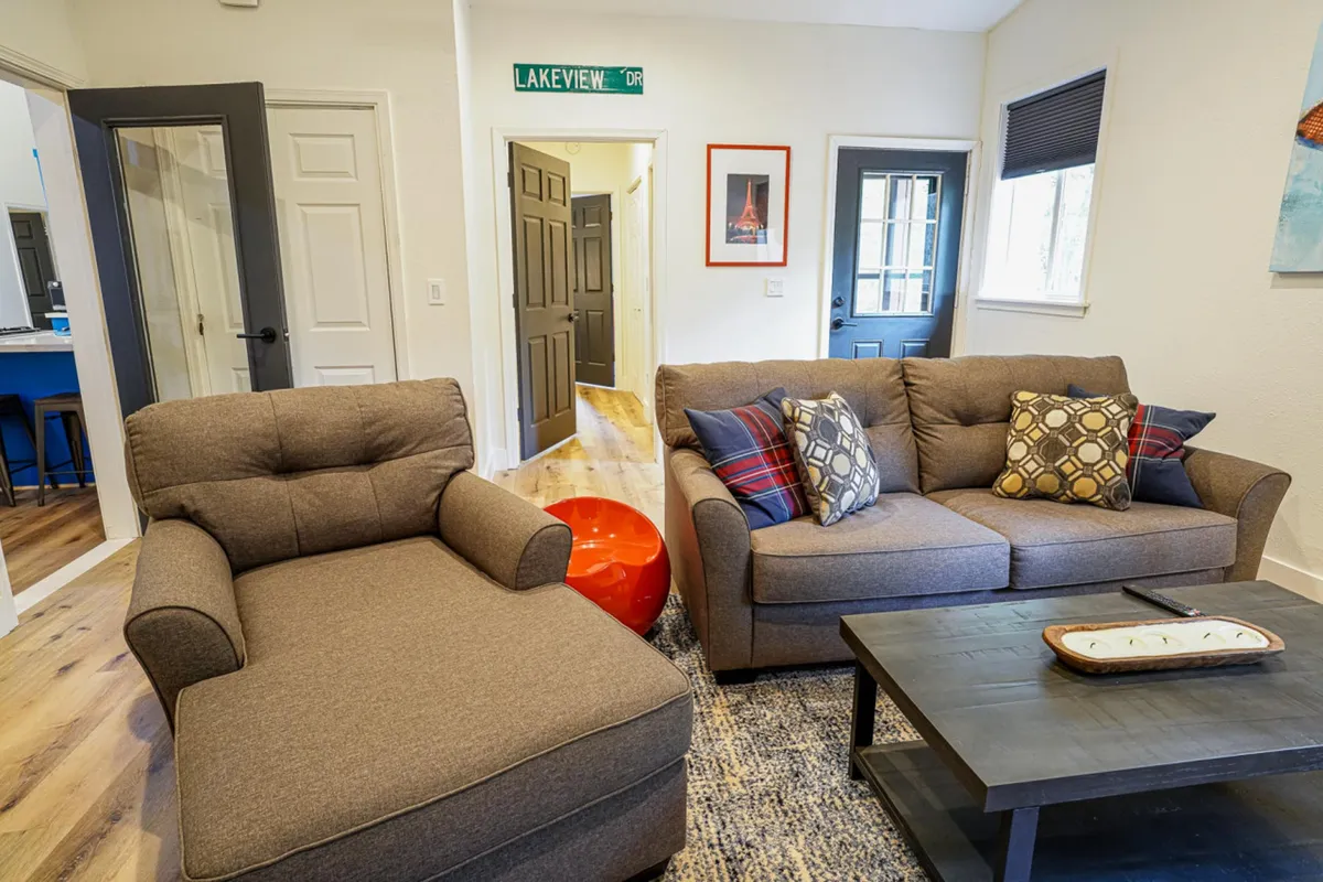 This image features a brown sectional sofa accented with decorative pillows, a red accent table, and framed Eiffel Tower artwork on the wall. The space is arranged for comfort and socializing, evoking a sense of warmth and inviting relaxation. The setup is ideal for group gatherings, casual conversations, or unwinding after outdoor adventures.